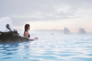 A woman soaking at the edge of steaming Myvatn Nature Baths surrounded by mist and lava rocks.