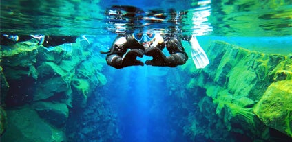 A person is making a heart with their hands as she snorkels between the tectonic plates of silfra in Iceland.