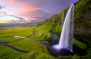 Seljalandsfoss waterfall seen on a sunny summer day with green grass surrounding it.