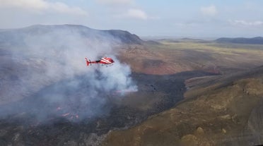 A red helicopter hovers above a steaming lava field at Fagradalsfjall Volcano on Reykjanes Peninsula.