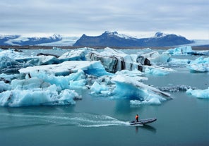 A small boat cruises through floating icebergs in Jokulsarlon Glacier Lagoon in southeast Iceland on a cloudy day.