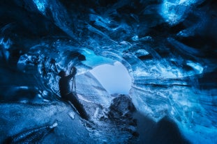Man takes photos in a glowing blue ice cave in Vatnajokull Glacier, South Iceland.