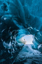 Inside a crystal blue ice cave in Vatnajokull National Park, a person stands on the icy edge.