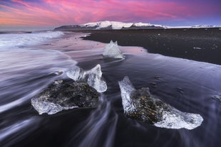 Glacier ice glistens on the black sand of Diamond Beach at sunrise in southeast Iceland.
