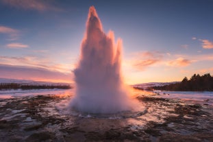 The Strokkur geyser erupts dramatically at sunset in the geothermal area of Haukadalur, part of Iceland's Golden Circle.
