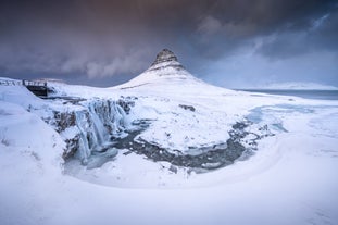 Mt. Kirkjufell is covered in snow during winter. Its distinctive pyramid shape stands tall, surrounded by a snowy landscape.