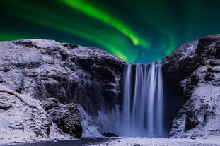 Northern lights glow above the snow-covered Skogafoss Waterfall on the South Coast of Iceland.