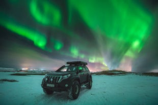 A 4x4 car parked on snowy terrain under vibrant northern lights in Iceland’s winter night sky.