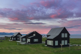 南アイスランドの紫がかったピンクの夕空の下、緑豊かな野原に佇む歴史あるアイスランドの芝屋根の家々。