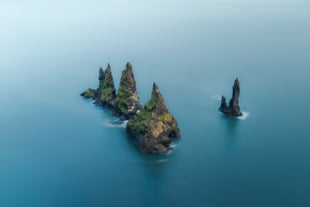 Reynisdrangar sea stacks rise dramatically from the ocean along Iceland’s south coast under a calm summer sky.