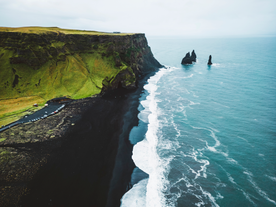 Waves crash along the black sand shore of Reynisfjara Beach near Vik, Iceland, with Reynisdrangar sea stacks in view.