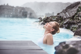 A woman is relaxing in the geothermal, mineral-rich waters of the Blue Lagoon, surrounded by snow.