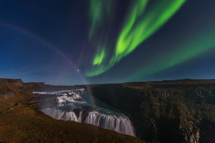 The northern lights shine over Gullfoss Waterfall in Iceland's Golden Circle, with a rainbow in the mist.