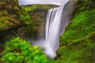 Skogafoss Waterfall cascades over a mossy cliff into a misty basin on Iceland’s South Coast.