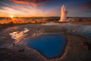 A powerful geyser erupts at sunset beside a steaming geothermal pool in Iceland’s famous Geysir geothermal area.
