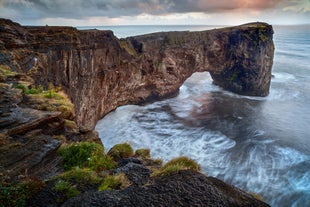 Le promontoire de Dyrholaey s'étend dans l'océan sous un ciel d'été nuageux, avec des falaises vertes et des vues côtières spectaculaires.