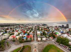 Aerial view of Reykjavik with colorful rooftops, city streets, and a rainbow arching over the skyline and harbor.